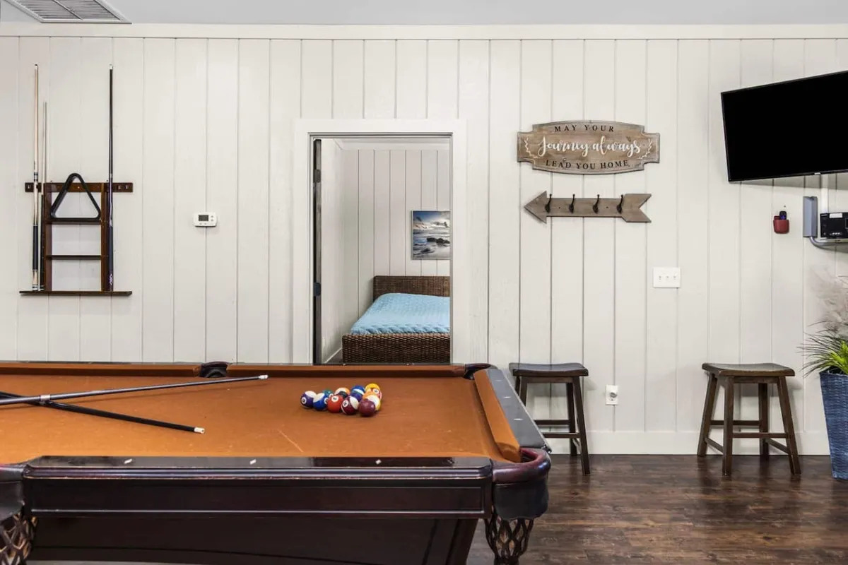 A dedicated game room featuring a pool table, seating stools, TV, and wall sign, all set in a casual and welcoming environment. This space exudes friendly competition and group fun, ideal for post-nightlife entertainment.