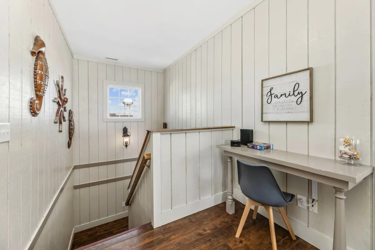 A naturally lit corner with a desk and chair, set beside a window. Wooden wall decor and a 'family' sign create an inviting, homey workspace, ideal for focused work or creative sessions while staying connected in comfort.