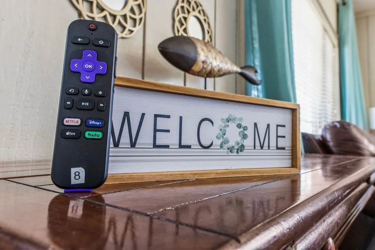 A close-up shot with a remote control, welcome sign, and decorative fish, subtly referencing the entertainment options available, such as a Smart TV for movies or sports. The cozy setup suggests a space designed for group enjoyment and relaxation.