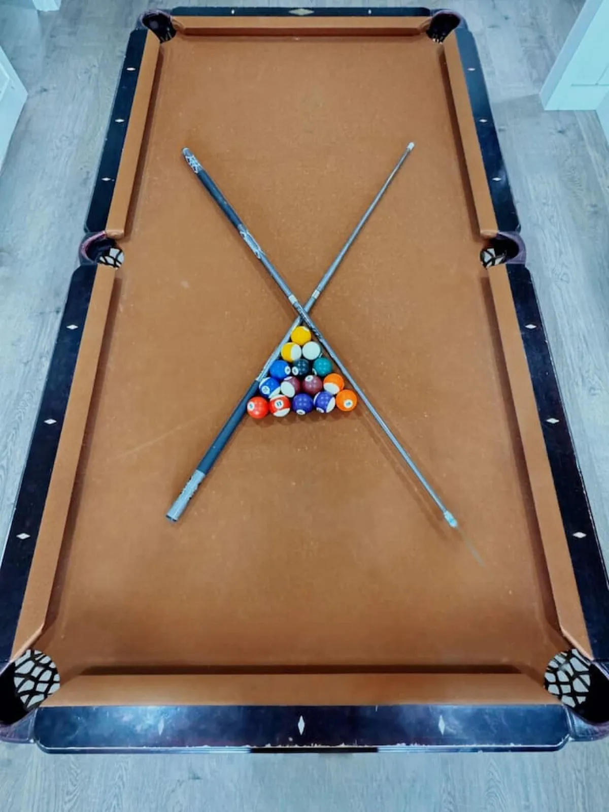 A cozy game room featuring a pool table set for play, with cue sticks arranged neatly along the wall. The relaxed atmosphere suggests a space designed for friendly competition and group interaction, ideal for team-building activities.